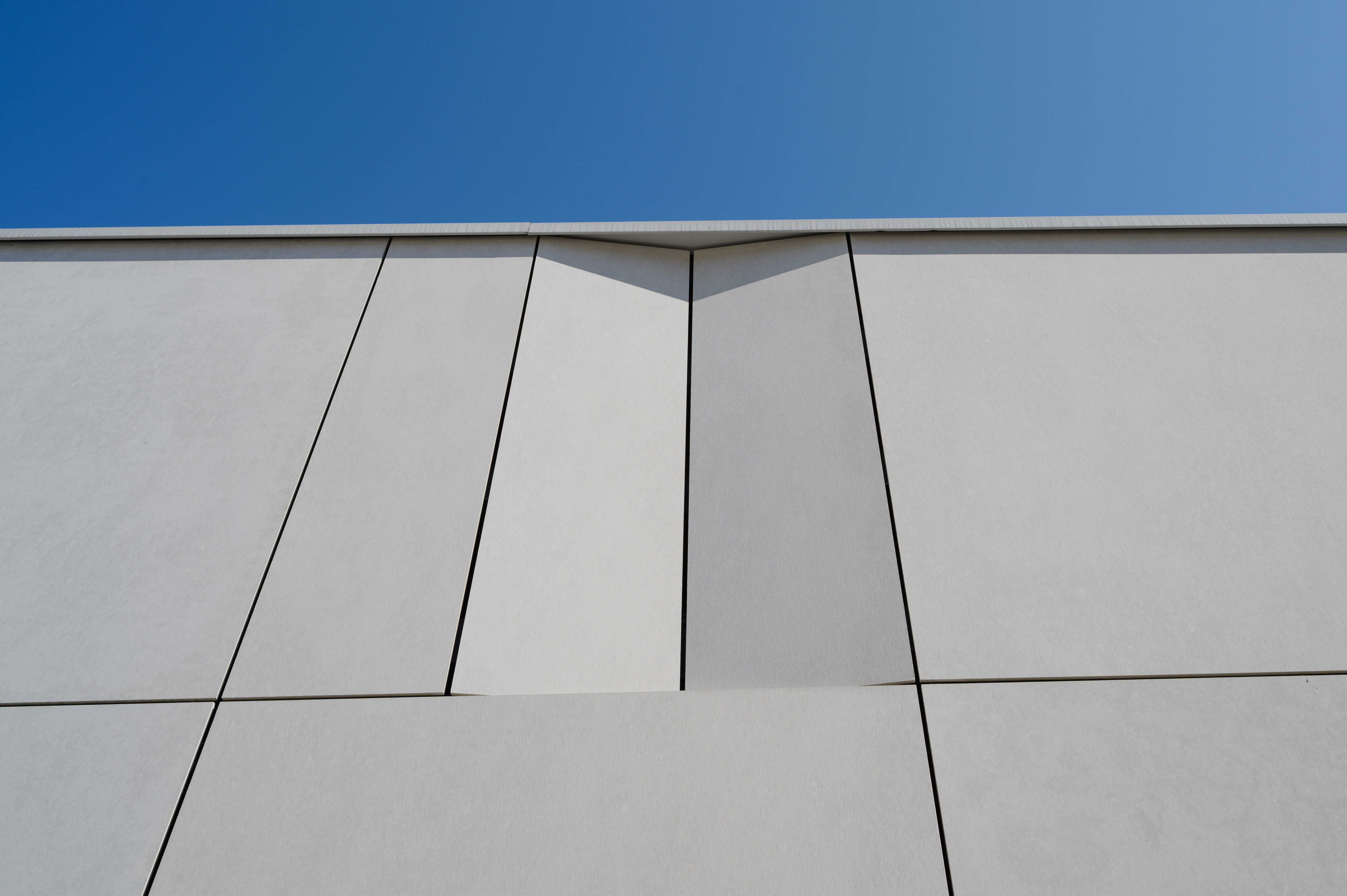 This image shows a close-up of an exterior facade clad with EQUITONE panels in a light grey tone. The panels are sleek and precise, with clean, sharp lines and subtle texture, highlighting the minimalist design. The joints between the panels create geometric patterns, enhancing the modern aesthetic. The light grey color contrasts beautifully with the clear blue sky, showcasing the smooth, refined look of EQUITONE's high-quality fiber cement material.